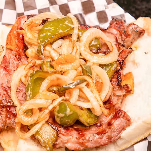 Close-up of a Moody's Pub steak sandwich with grilled onions and green peppers on a bun.